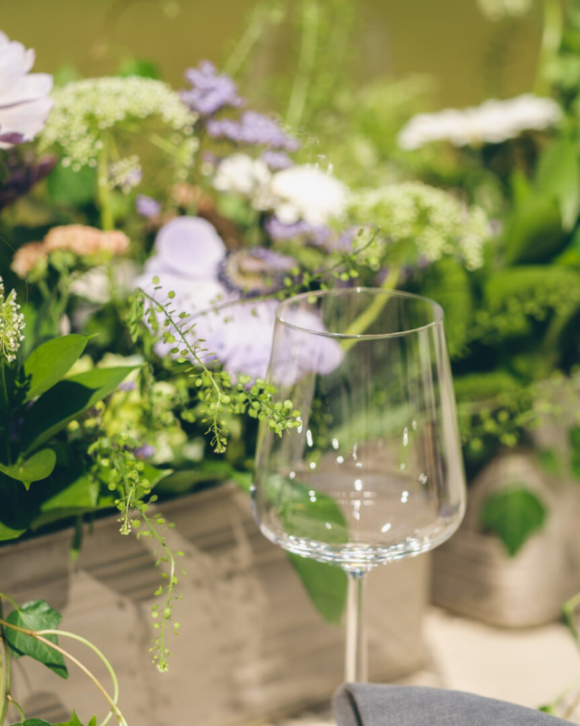Ett vinglas vid krukor med blommor.